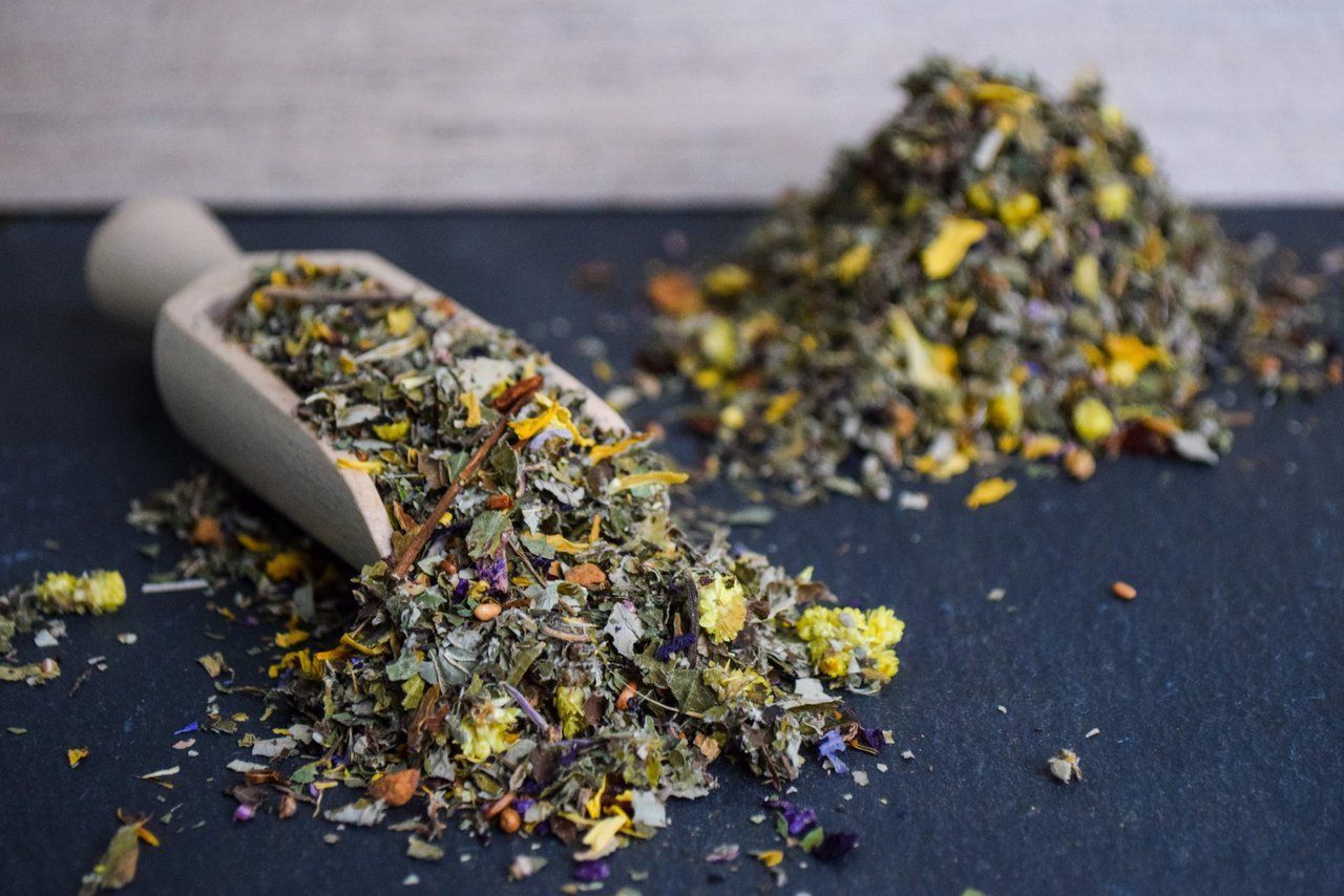 Lose, gesprenkelte Teeblätter fielen aus einer kleinen Schaufel auf eine dunkle Oberfläche.