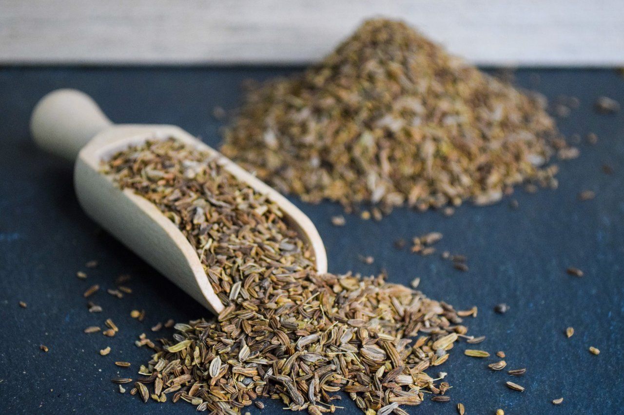 Eine weiße Schaufel gefüllt mit getrockneten Kräutern neben einem kleinen Haufen auf einer dunkelblauen Oberfläche