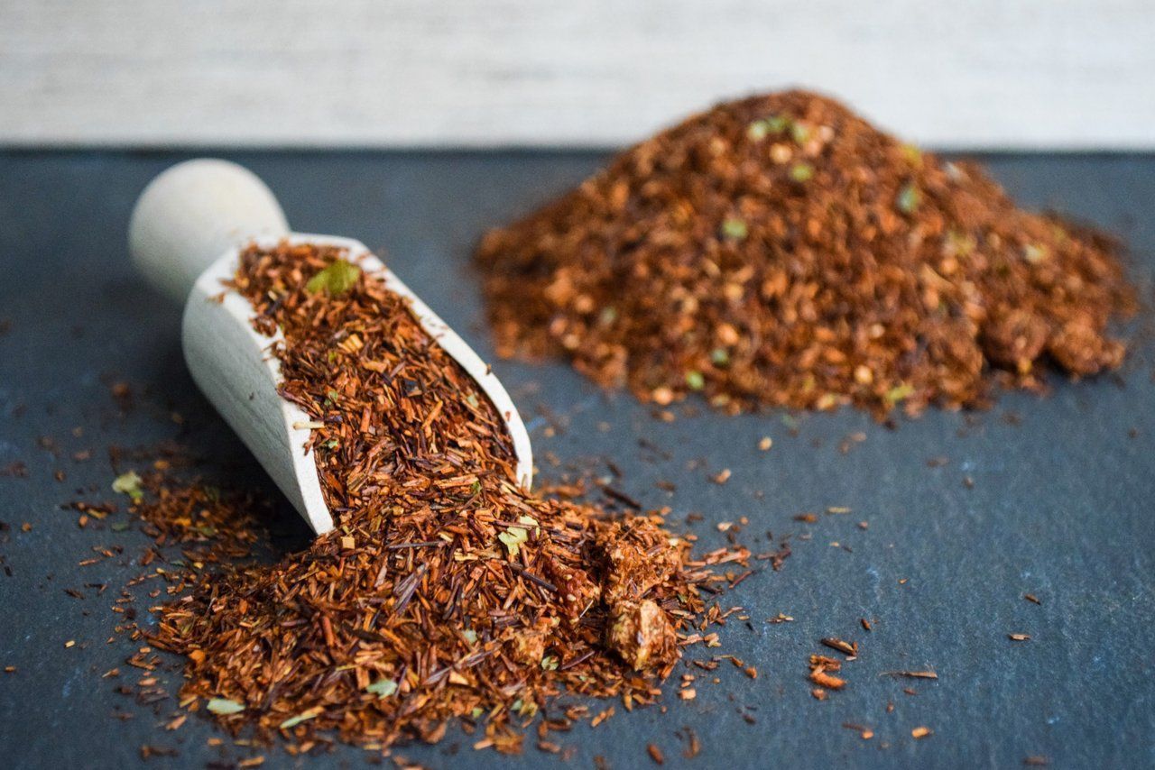 Zwei weiße Löffel verschütten losen rotbraunen Tee auf eine graue Oberfläche.