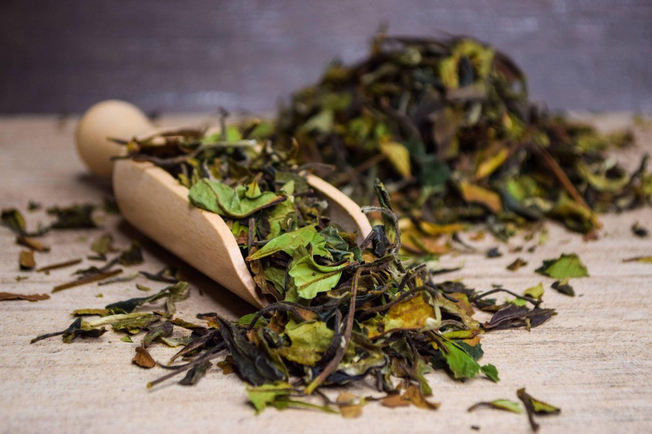 Papiertüte, aus der getrocknete Teeblätter auf eine Holzoberfläche fallen.