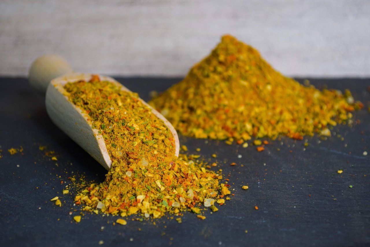 Eine Holzschaufel verschüttet bunte Gewürzmischung neben einem Hügel auf dunkler Oberfläche.