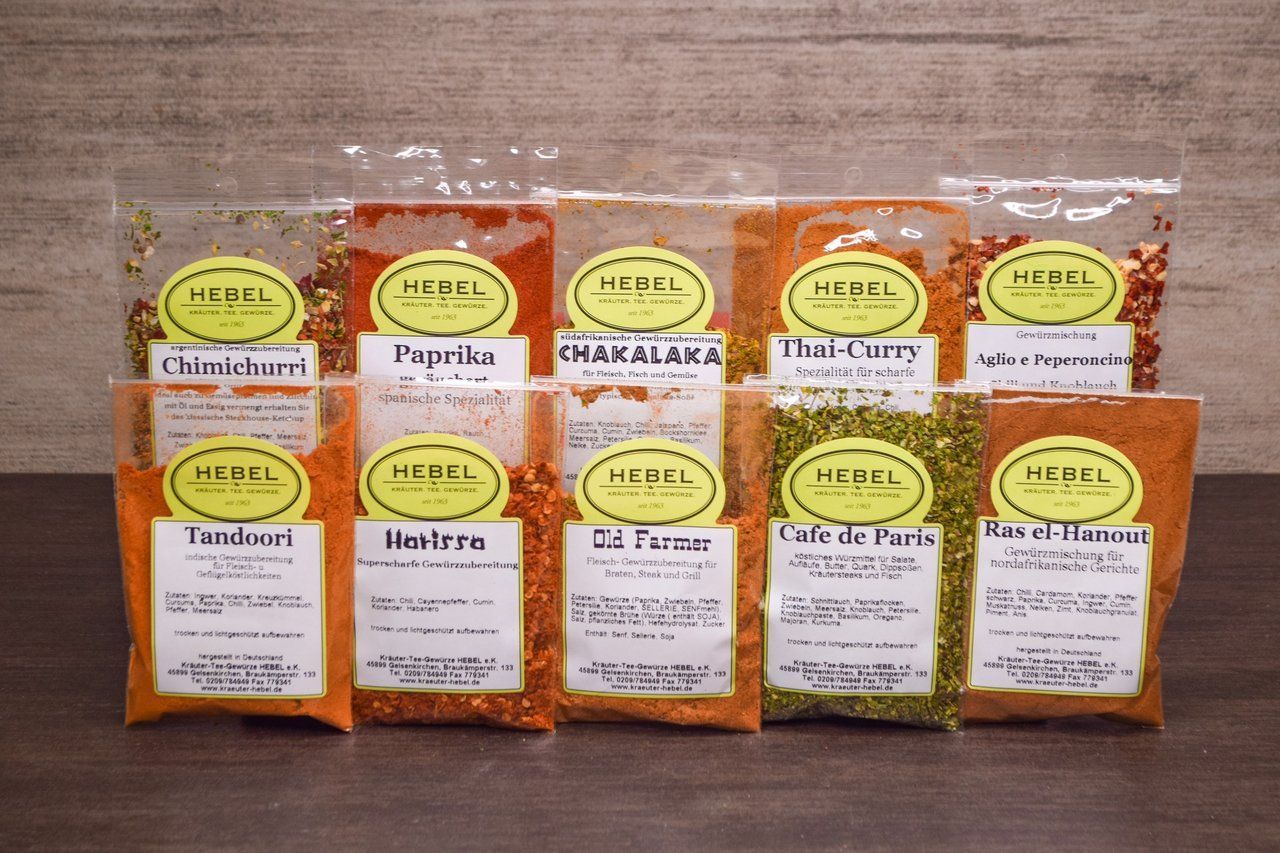 Verschiedene Gewürzpäckchen mit handgeschriebenen Etiketten lagen in Reihen auf einer Holzoberfläche.