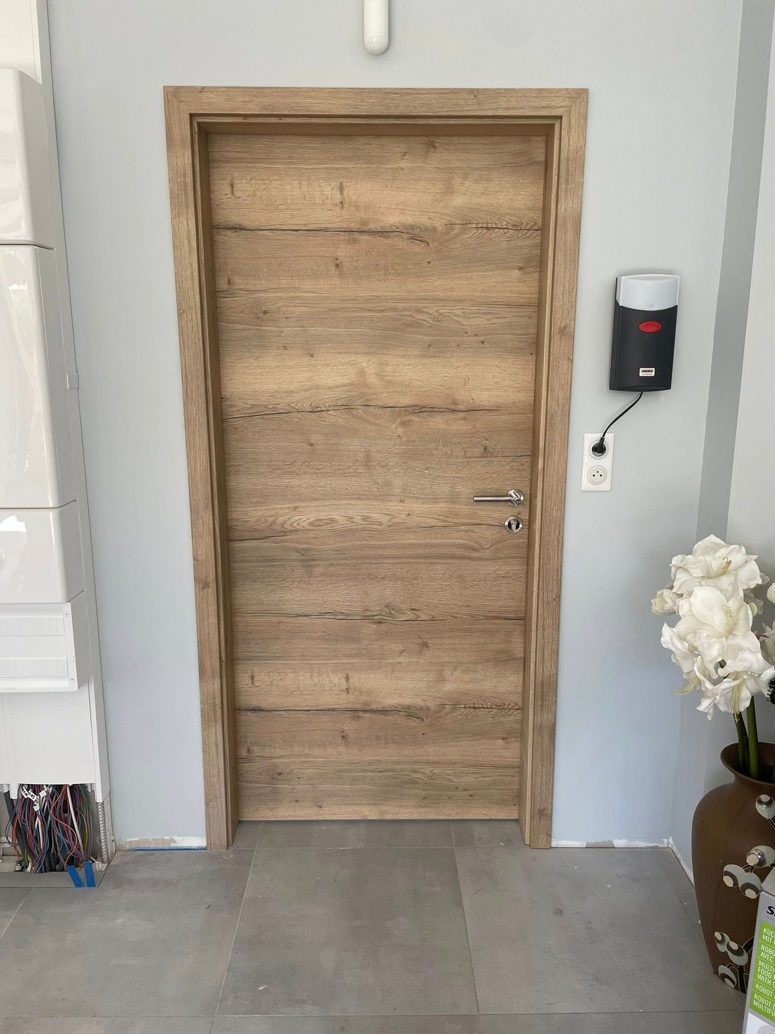 Porte intérieure en bois dans une pièce peinte en gris, avec un ouvre-porte automatique fixé au mur.