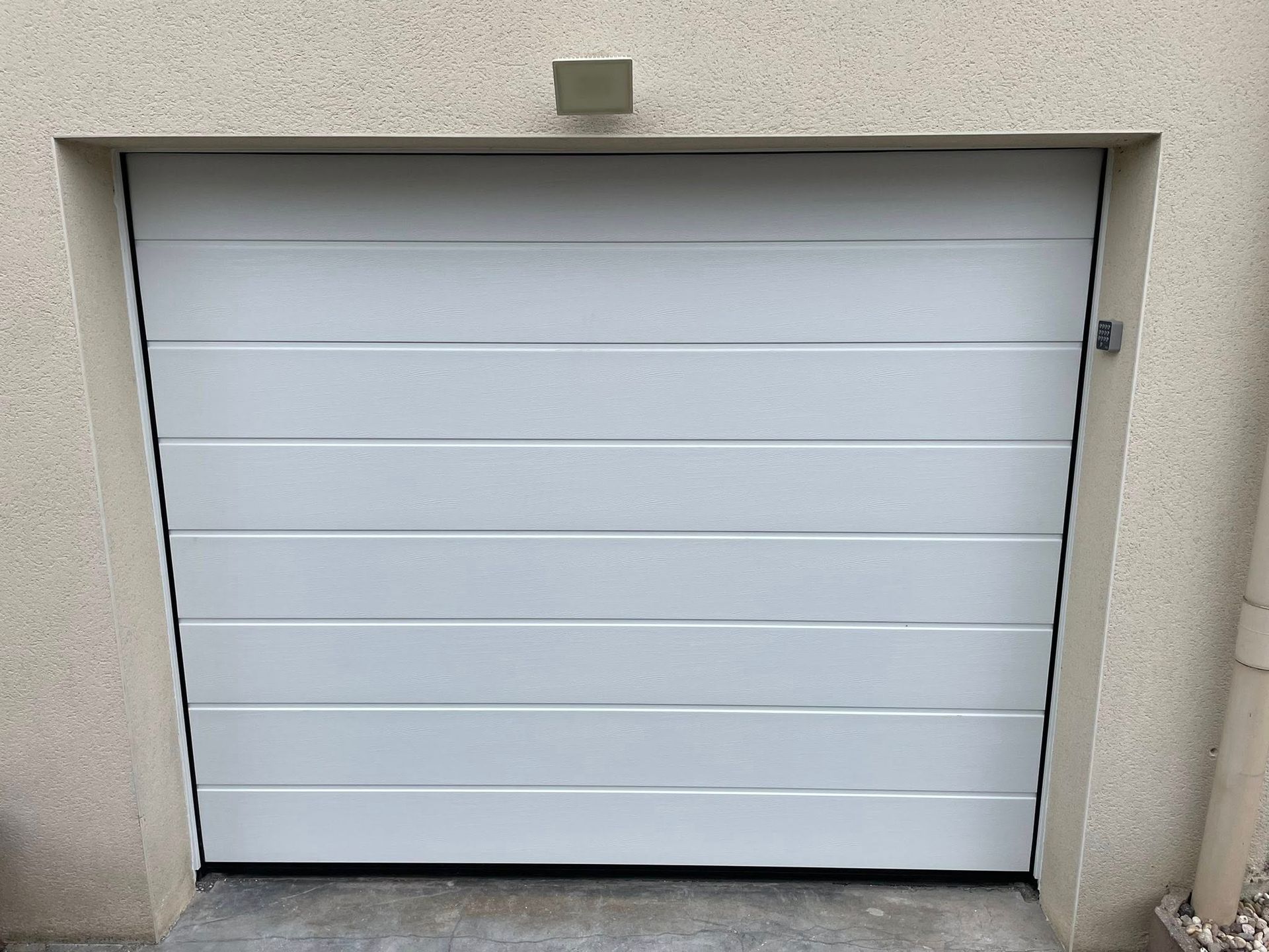 Porte de garage à panneaux horizontaux blancs, entourée de murs beige clair.