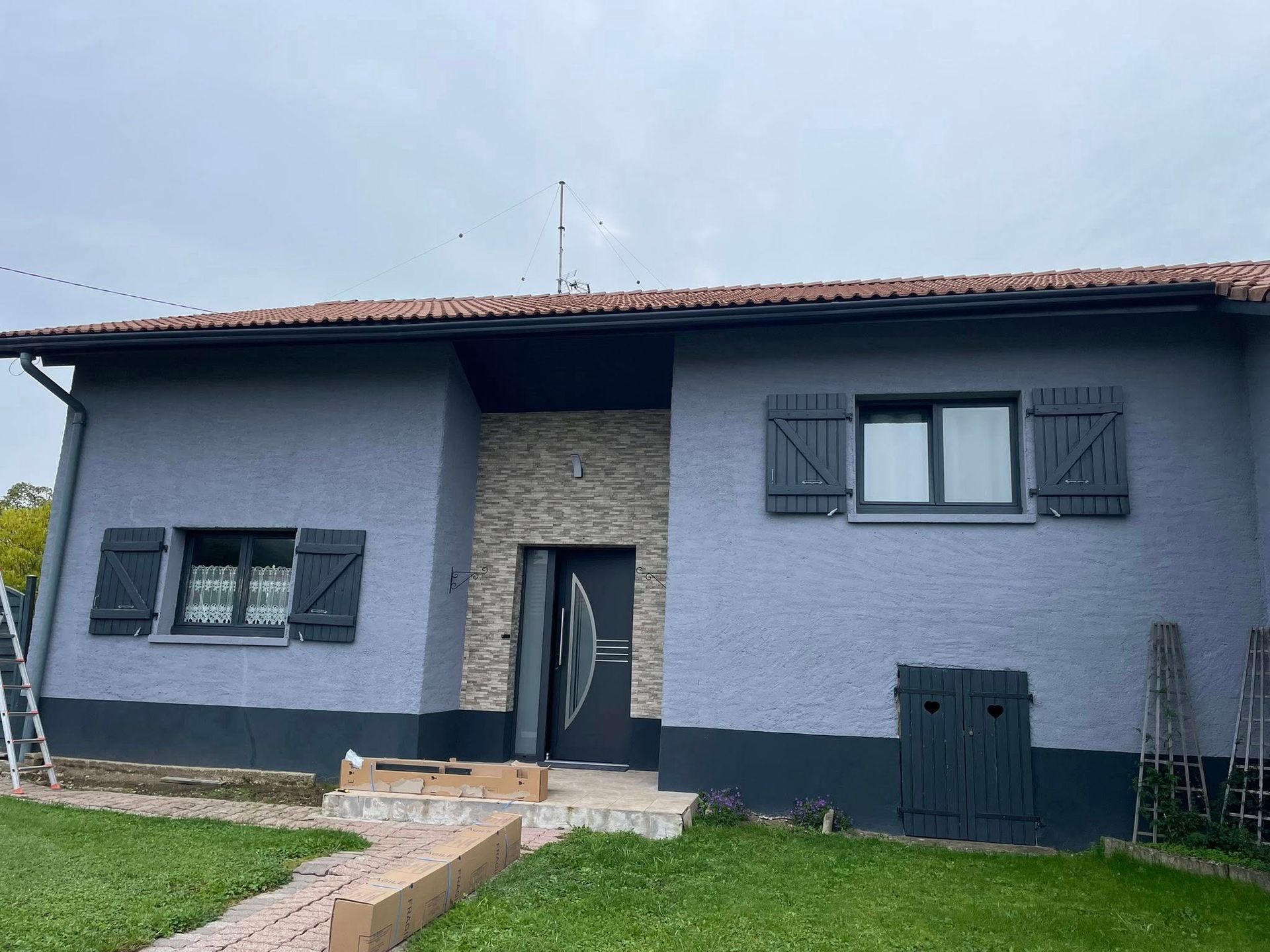 Une maison peinte en gris avec des boiseries et des volets gris foncé. L'entrée est dotée d'une façade en pierre.