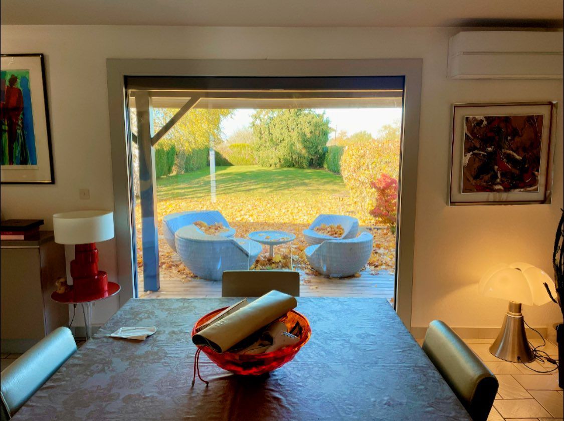 Vue à travers une porte avec une table à manger au premier plan, deux chaises et une table sur une terrasse.