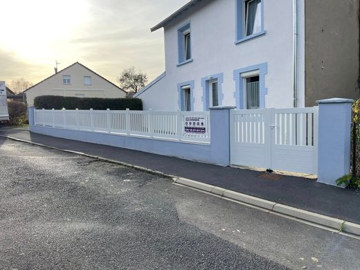 Clôture et portail blancs devant une maison bleu clair, au bord d'une rue.