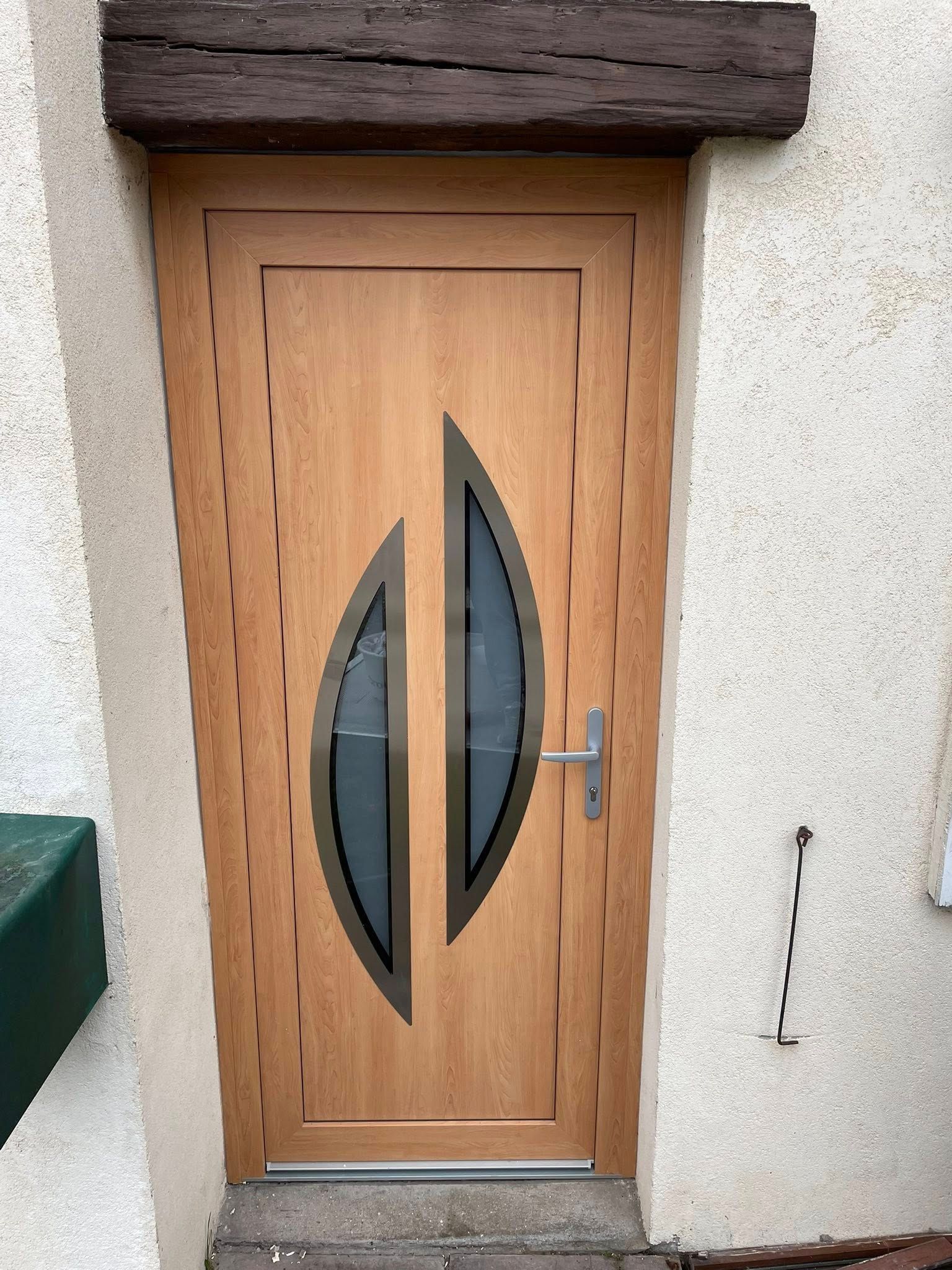 Porte beige avec panneaux de verre ovales, poignée argentée, poutre en bois au plafond.