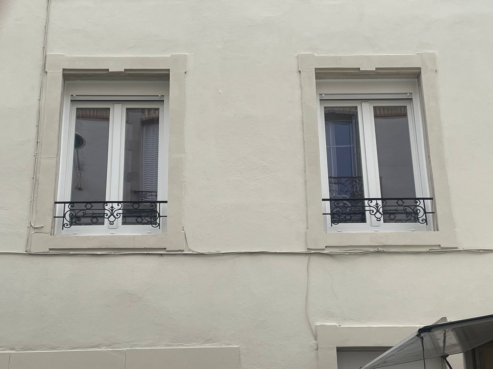 Fenêtre blanche avec volet roulant blanc fermé, en milieu urbain.