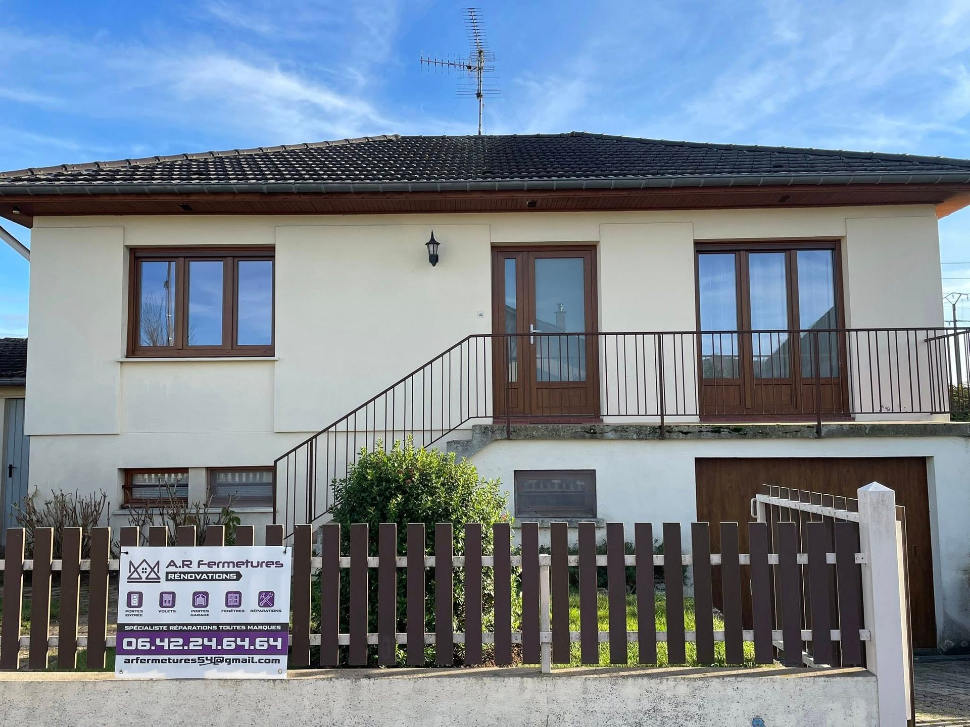 Extérieur de la maison avec des boiseries, des fenêtres et une porte marron, comprenant un petit balcon et une clôture en bois marron à l'avant.