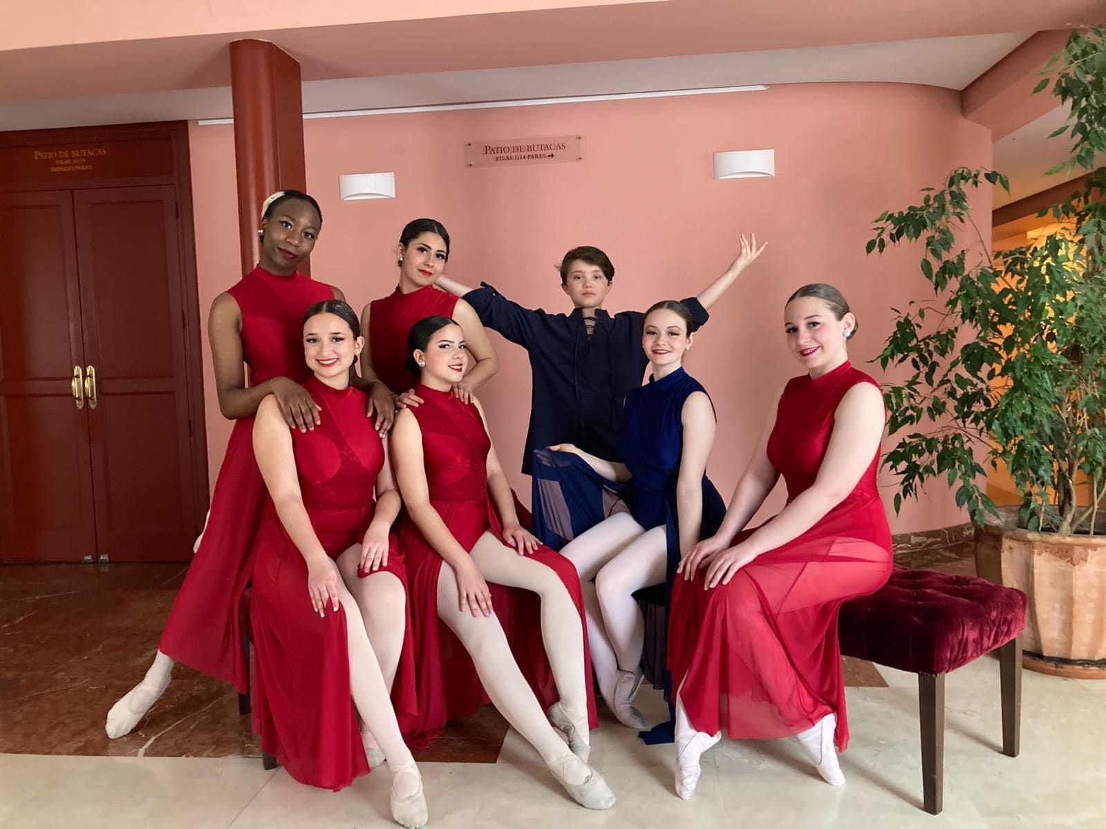 Grupo de bailarines de ballet con trajes rojos y azules posando para una foto en el interior.