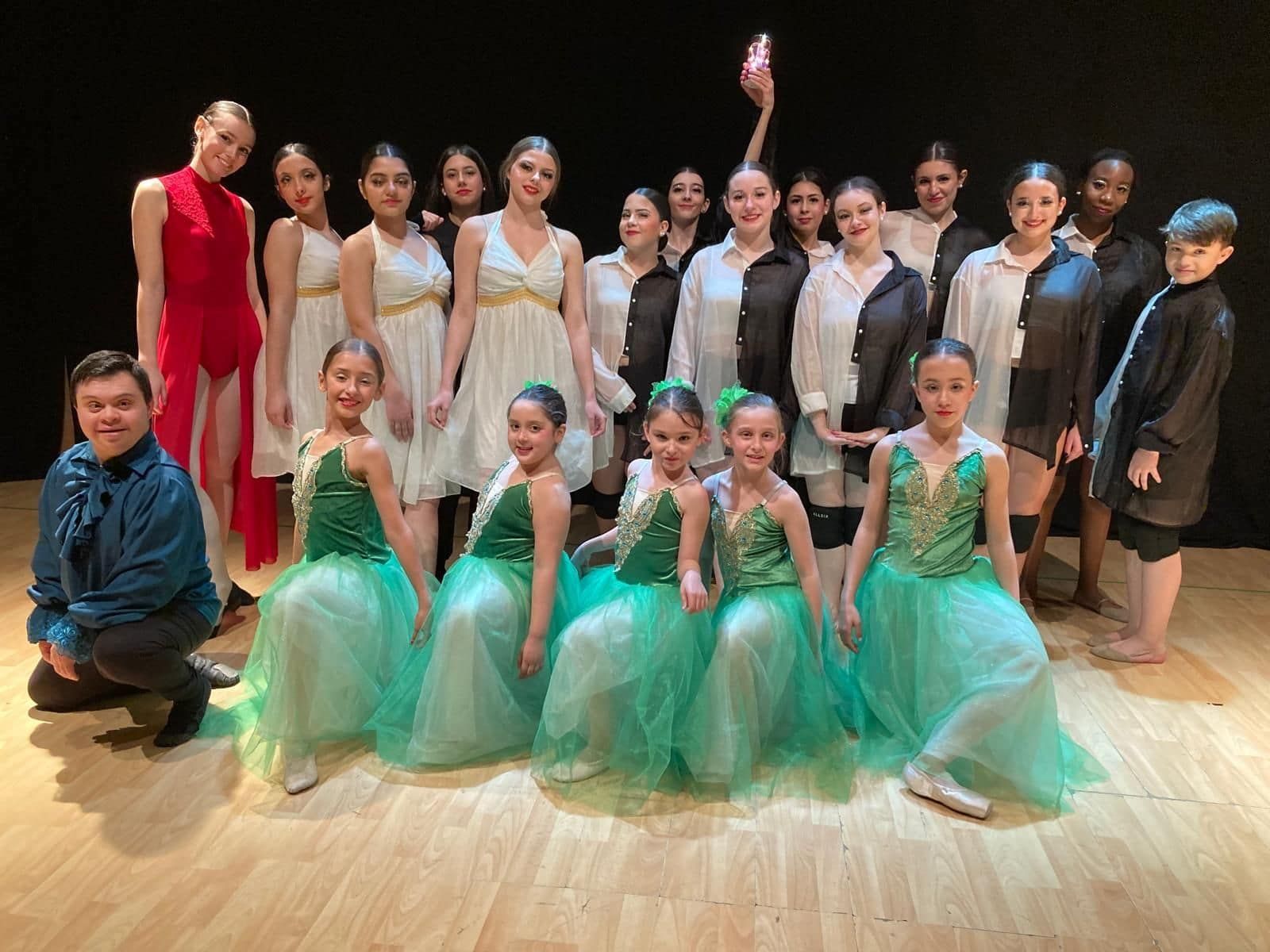 Grupo de bailarines en el escenario, varios trajes, fondo negro, suelo de madera.