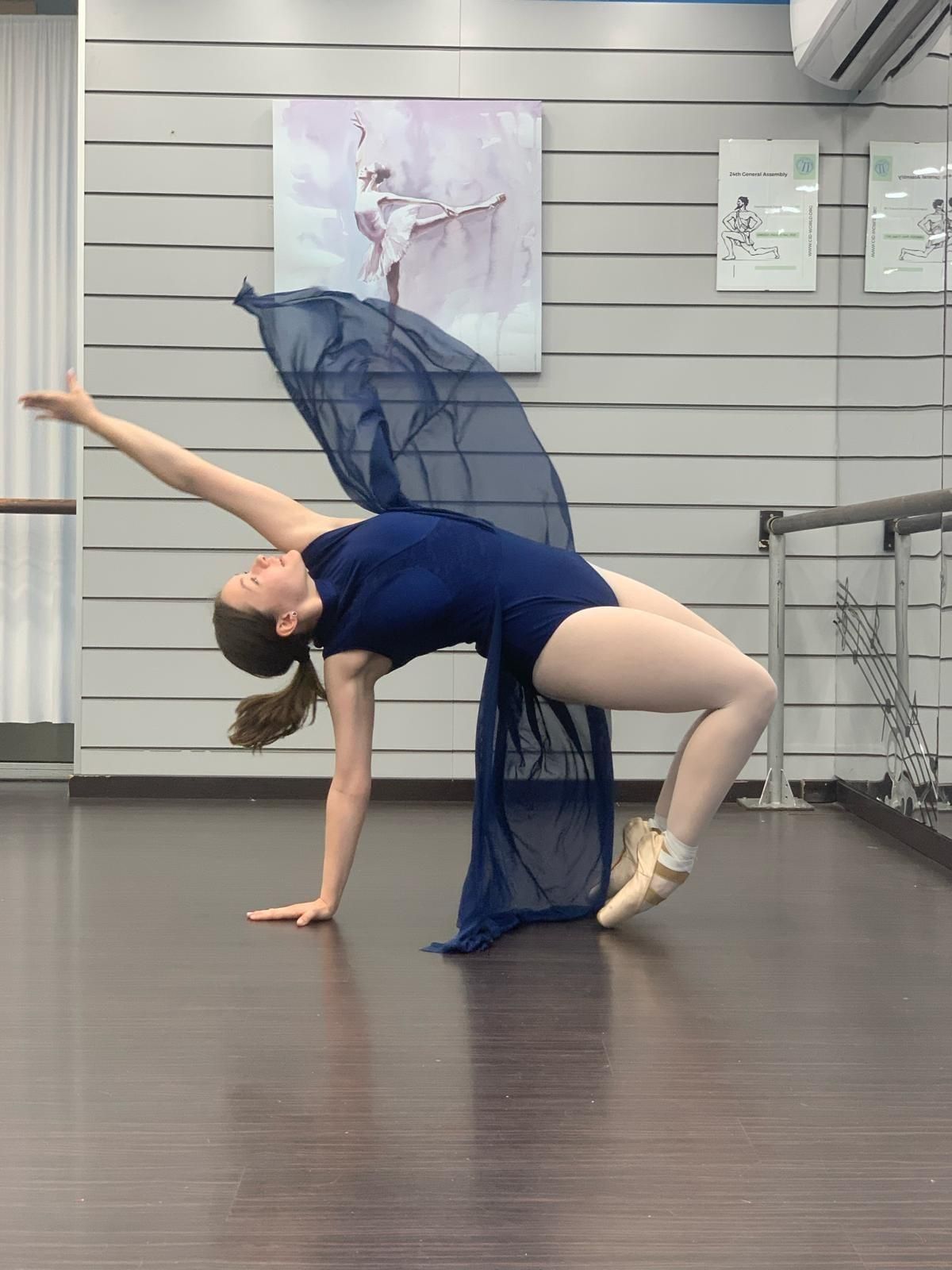 Bailarina en pose de puente, leotardo azul, tela fluida, estudio de ballet.