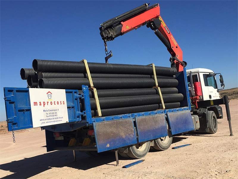 Una grúa está levantando una pila de tuberías desde la parte trasera de un camión.