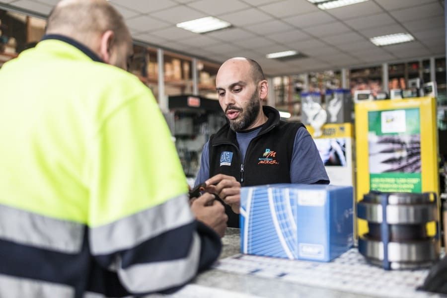 Un hombre está sentado en un mostrador de una tienda hablando con otro hombre.