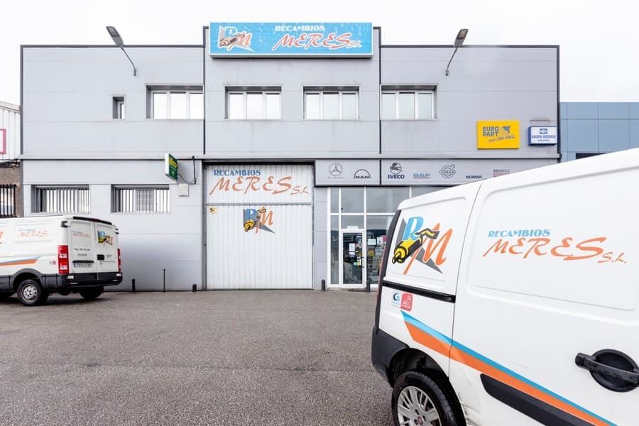 Dos camionetas blancas están estacionadas frente a un edificio que dice merisa