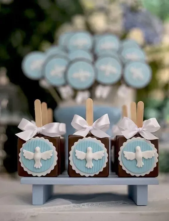 Tres cajas de dulces azules y marrones con lazos de cinta blanca y adornos de palomas sobre un pequeño soporte.