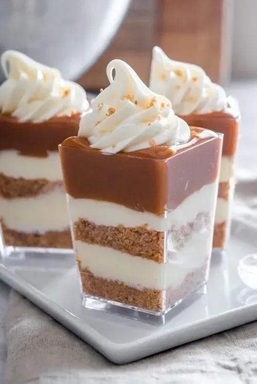 Vasitos de postre de caramelo en capas cubiertos con crema batida en una bandeja