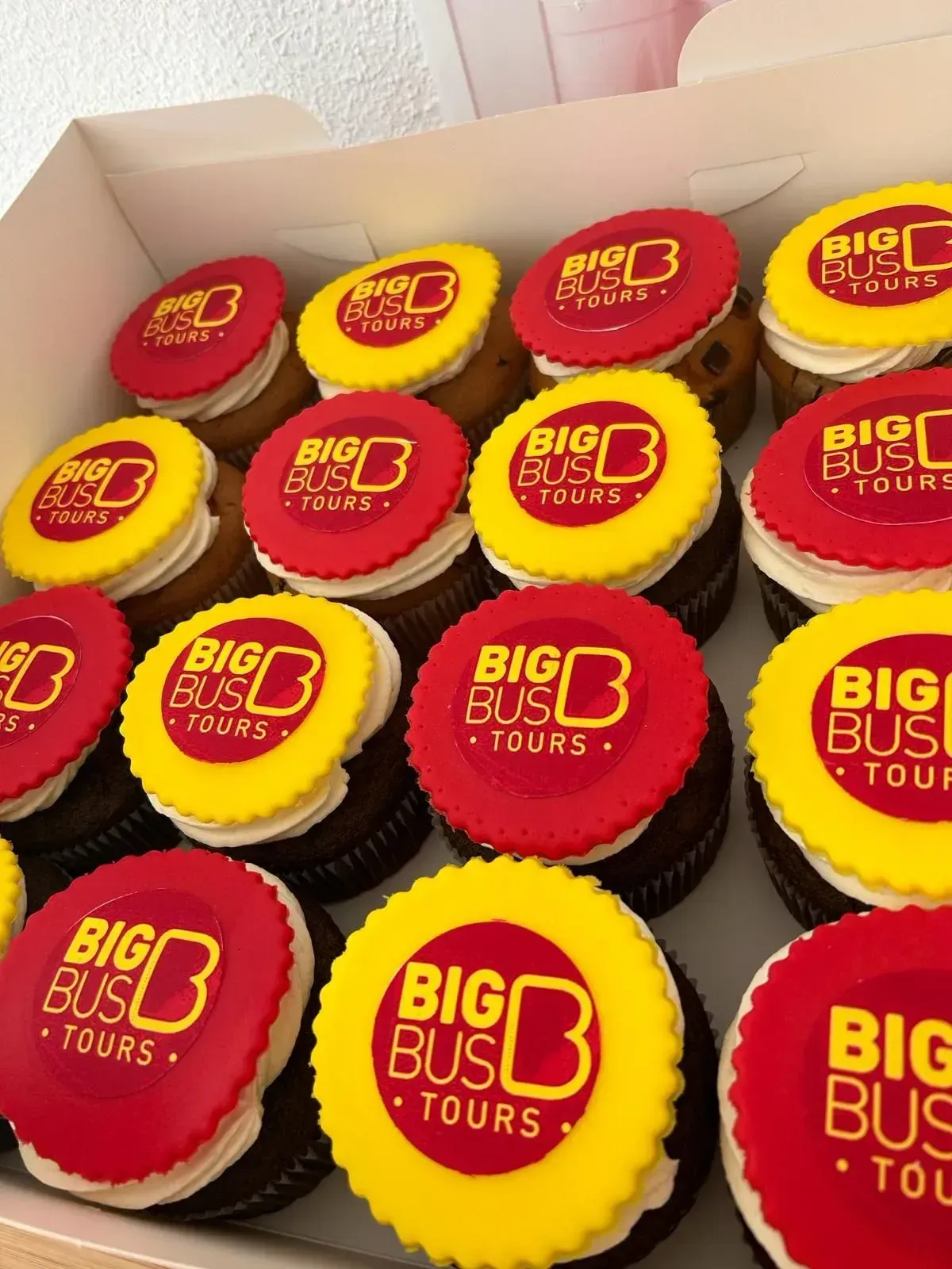 Caja de cupcakes rojos y amarillos de Big Bus Tours con base de chocolate