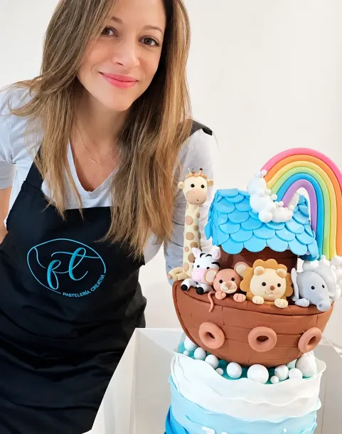 Mujer junto a un colorido pastel con temática de osito de peluche, decorado con un arcoíris y detalles de glaseado azul.