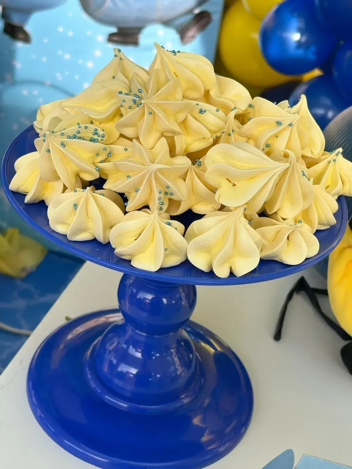 Soporte azul con forma de pedestal, coronado con magdalenas glaseadas de color amarillo y espolvoreadas con azúcar azul.