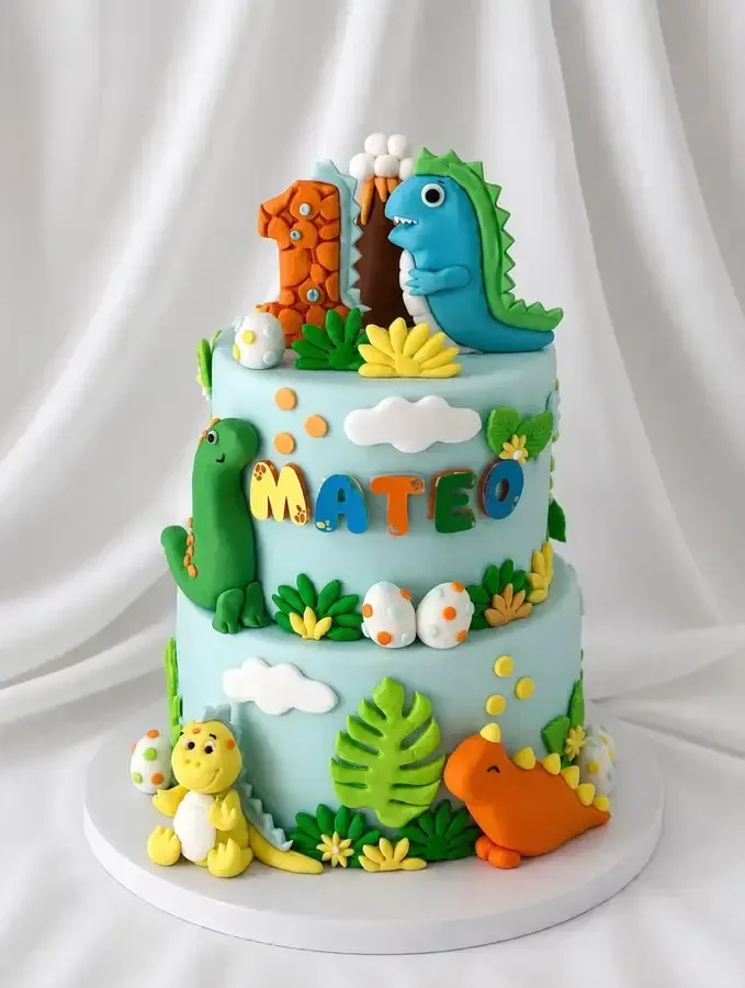 Tarta de cumpleaños de dinosaurio azul con dinosaurios verdes, nubes y letras coloridas sobre una base blanca.