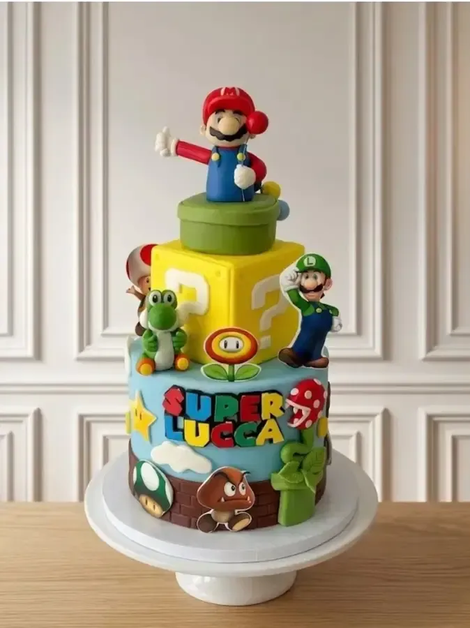 Tarta de cumpleaños amarilla con temática de Super Mario y adornos de personajes sobre una base blanca.