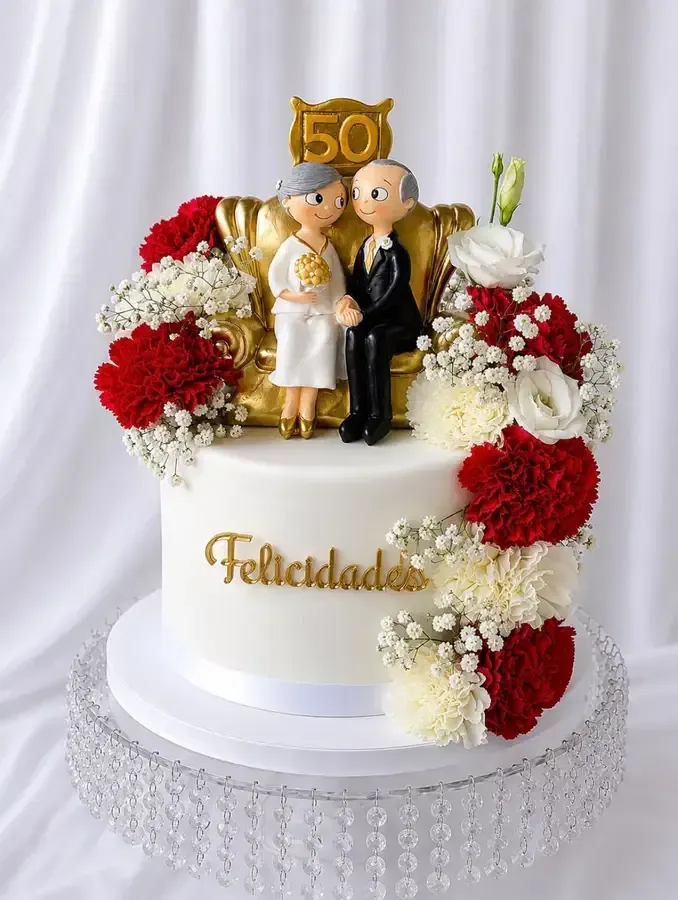 Adorno dorado para pastel de bodas sobre pastel blanco con flores rojas y blancas y texto “Felicidades”