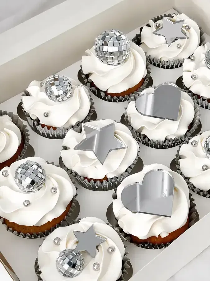 Magdalenas decoradas en plata y blanco con adornos en forma de corazón, dispuestas en una caja blanca.