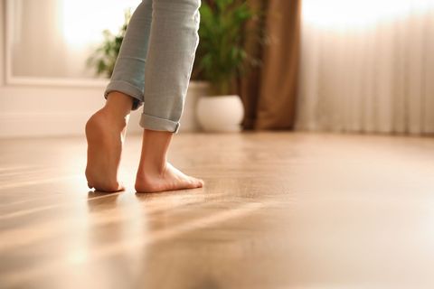 Représentation d'un plancher chauffant avec une jeune femme marchant dans son salon pieds nus.