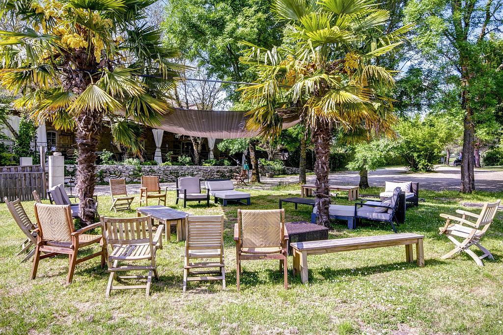 Un espace extérieur aménagé avec diverses chaises et tables en bois sous des palmiers.