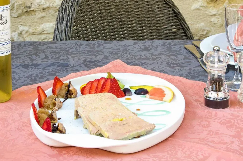 Assiette de fruits et de pâté sur une nappe rose, à côté de bouteilles de vin et de salières et poivrières.