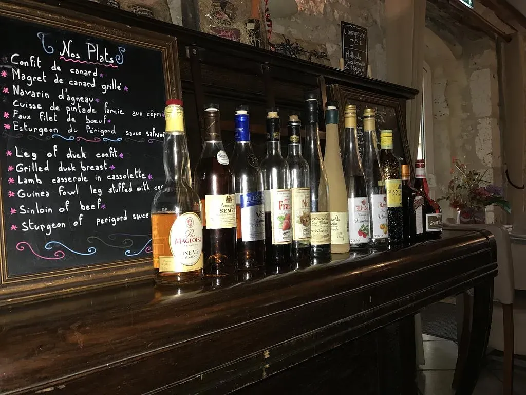 Des bouteilles d'alcool alignées sur un bar en bois sombre, un menu sur un tableau noir.