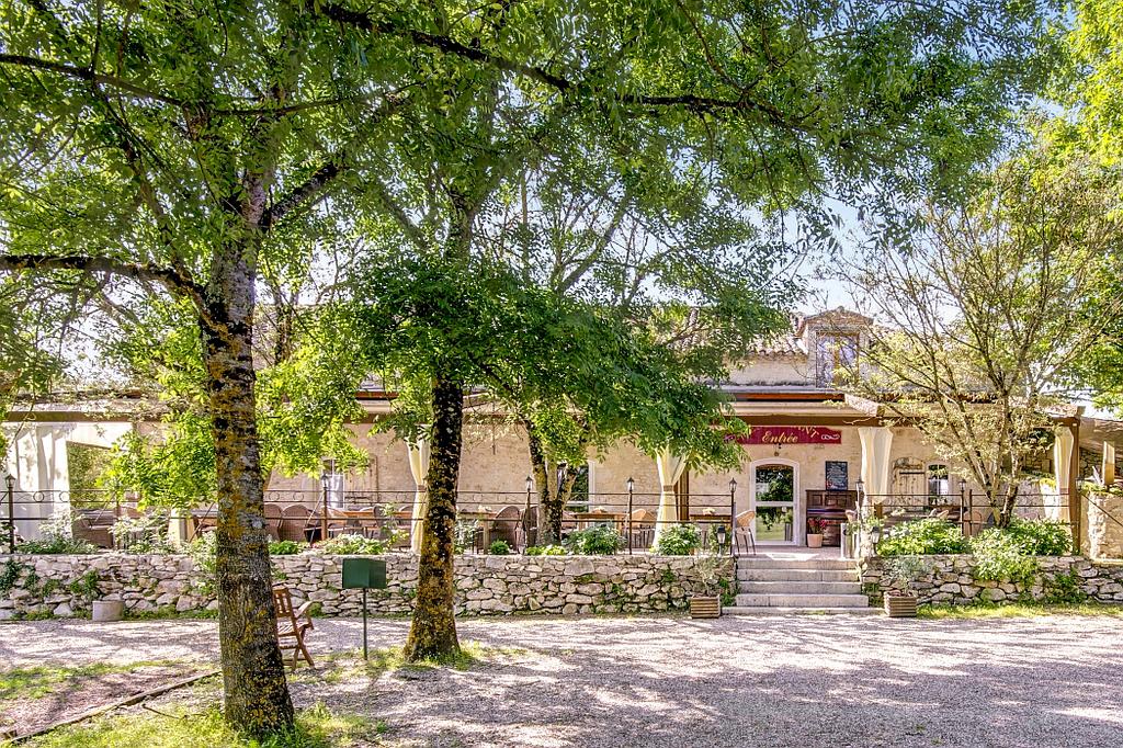 Extérieur du restaurant avec arbres et murs de pierre ; allée de gravier à l'avant.