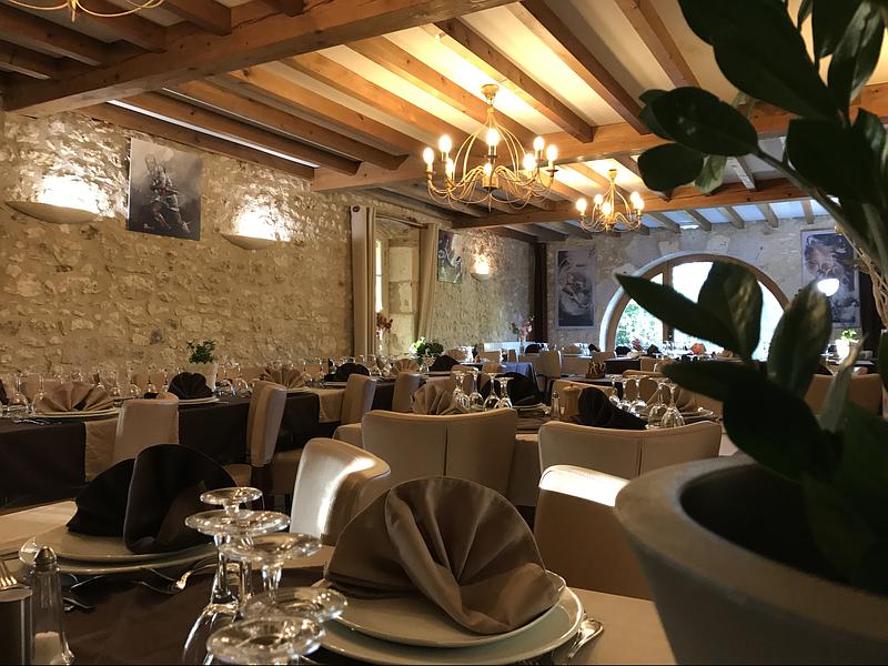 Intérieur du restaurant avec murs en pierre, poutres en bois, tables dressées et un lustre.