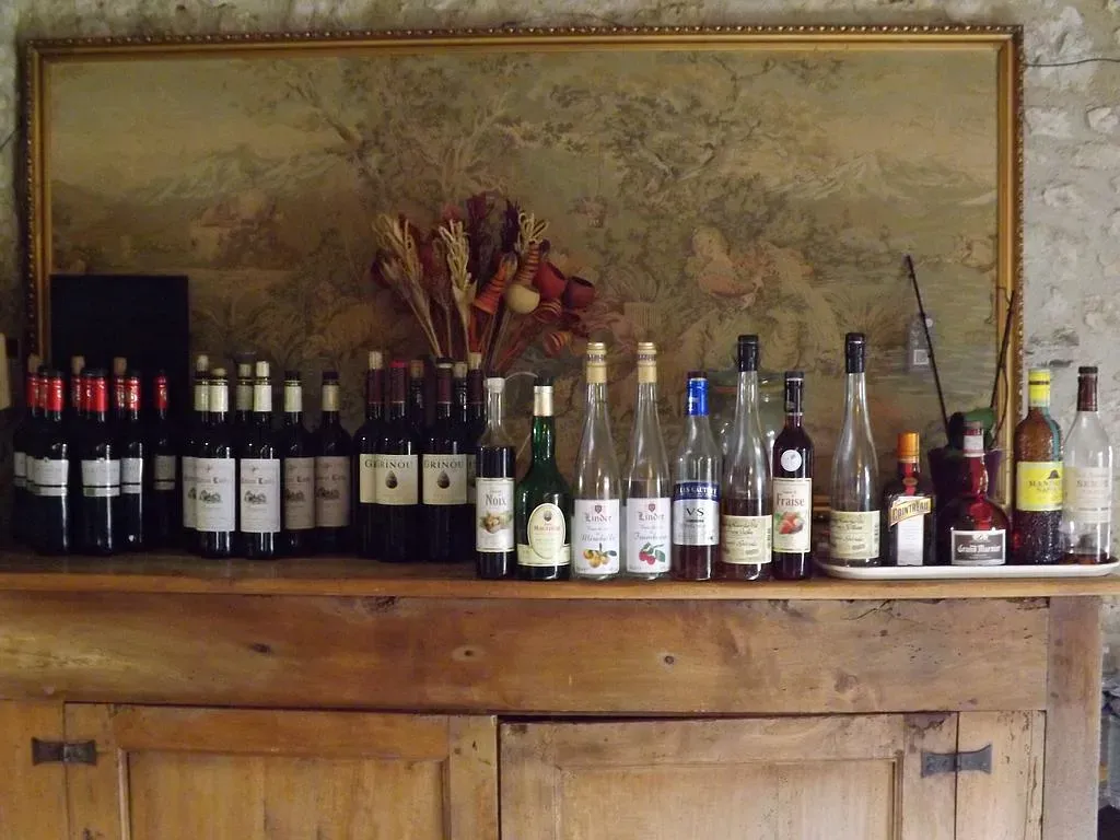 Des bouteilles de vin et autres boissons sur un buffet en bois, avec un tableau au-dessus et une composition florale.