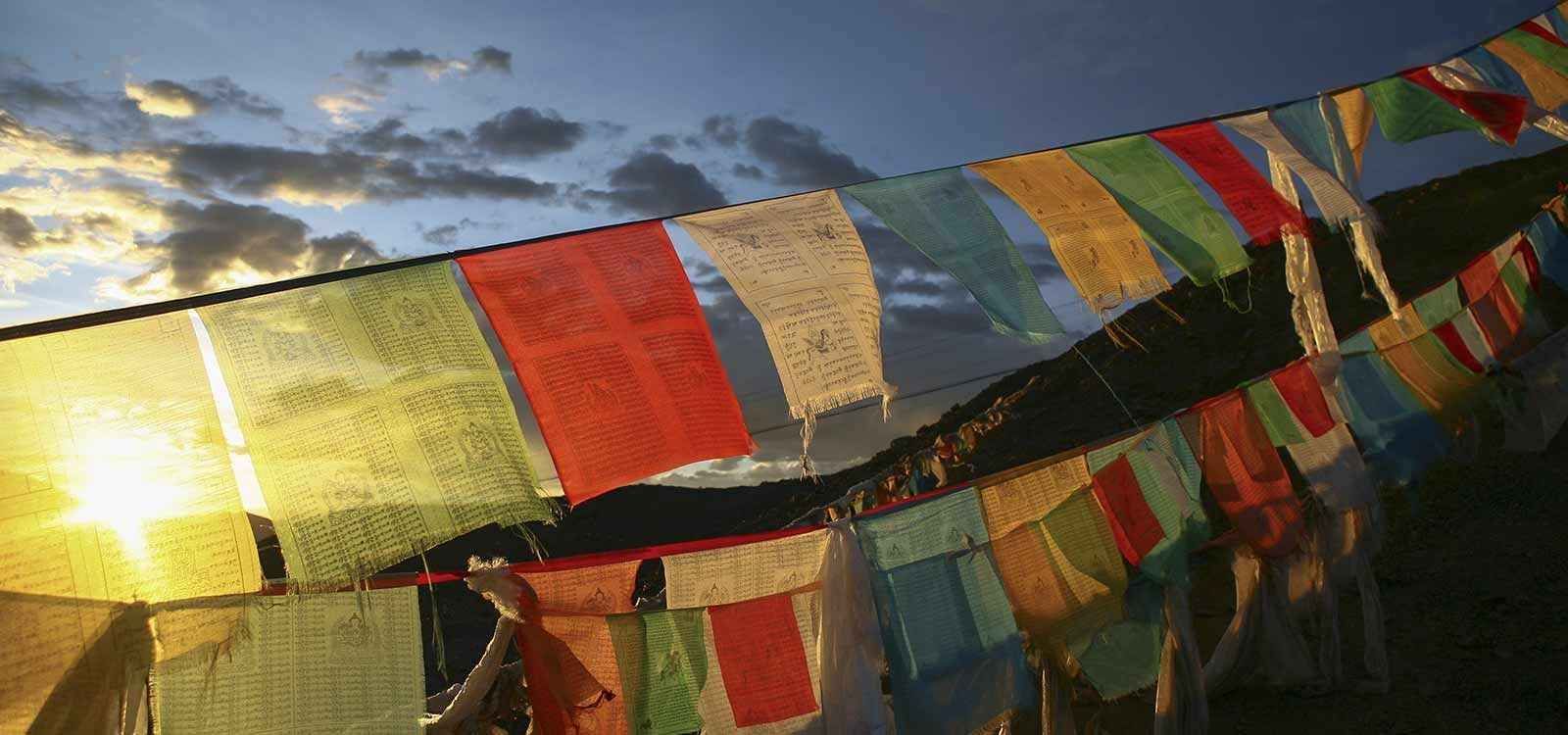 Una fila de coloridas banderas de oración colgando de una valla al atardecer.