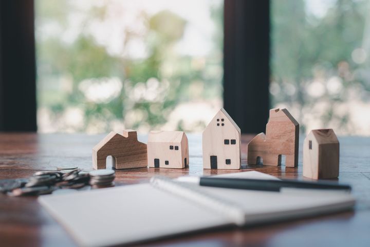 Una mesa de madera cubierta con casas de madera, monedas, un cuaderno y un bolígrafo.