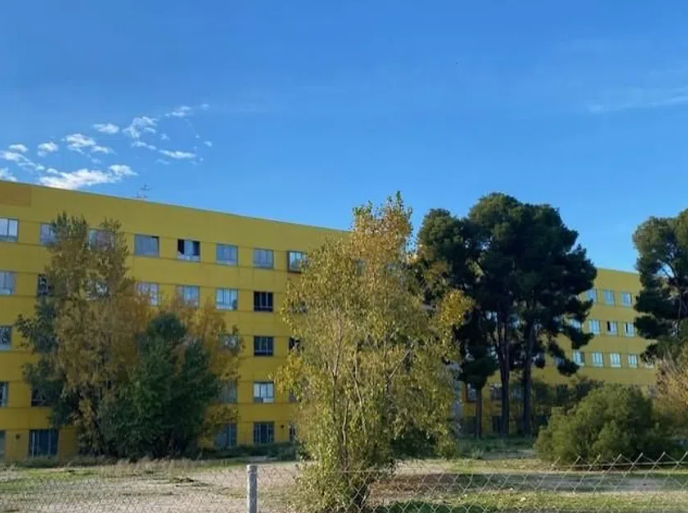 Un gran edificio amarillo con árboles delante.