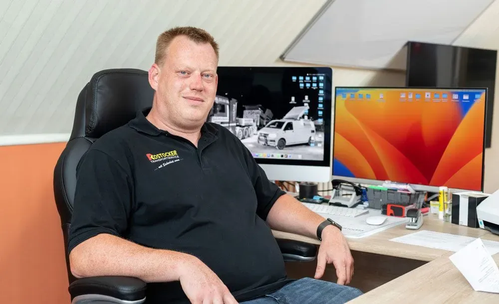 Ein Mann sitzt an einem Schreibtisch mit zwei Monitoren und Bürounterlagen in seinem Heimbüro.