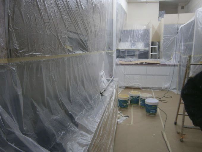 Habitación pintada en proceso de renovación, cubierta con láminas de plástico y con cubos de pintura en el suelo.