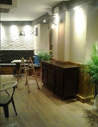 Interior acogedor de una cafetería con escalera, armario oscuro, plantas en macetas e iluminación de pared texturizada.