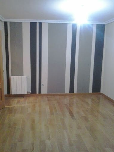 Habitación vacía con paredes grises a rayas, suelo de madera clara y una luz brillante en el techo.
