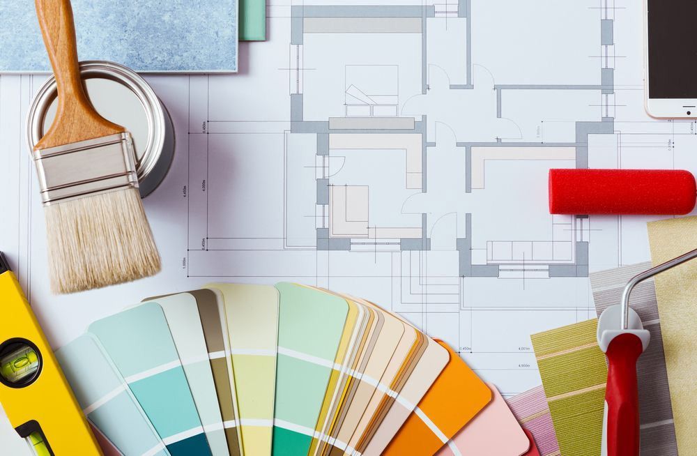 Herramientas de diseño de interiores con muestras de pintura, pincel, rodillo y plano sobre una superficie de trabajo.
