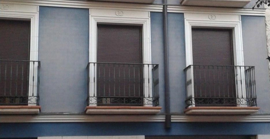 Tres balcones de apartamentos de color azul grisáceo con contraventanas cerradas y barandillas de metal oscuro.