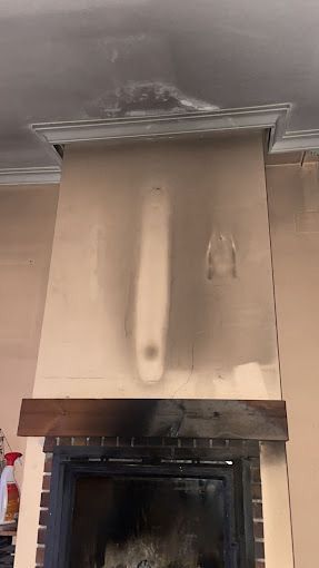 Una pared carbonizada sobre una chimenea con daños por humo y el borde del techo dañado.
