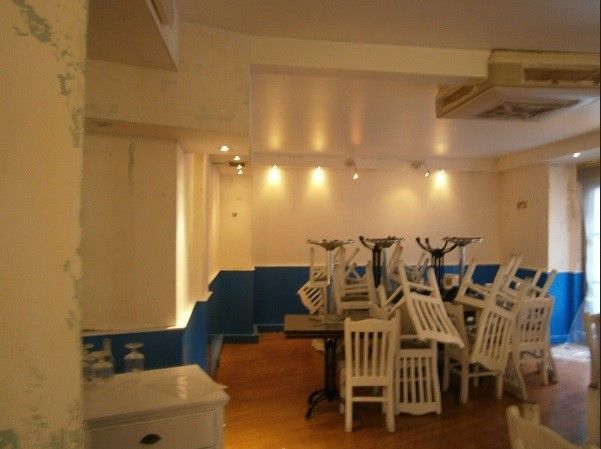 Comedor vacío de un restaurante con sillas blancas apiladas sobre las mesas y paneles de pared azules.
