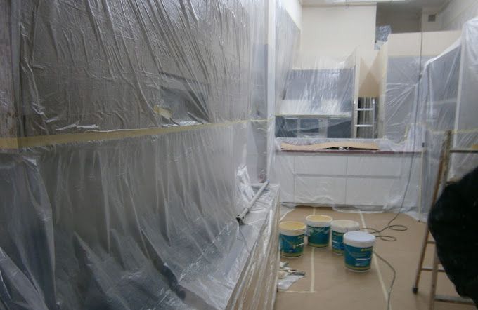 Habitación pintada con muebles cubiertos con láminas de plástico y varios cubos de pintura en el suelo.
