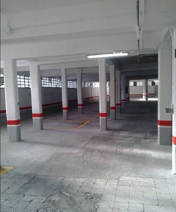 Garaje cubierto vacío con columnas blancas y bandas de seguridad rojas en las paredes y pilares.
