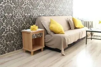 Acogedora sala de estar con un sofá beige, cojines amarillos, papel pintado estampado y una pequeña mesa auxiliar de madera.